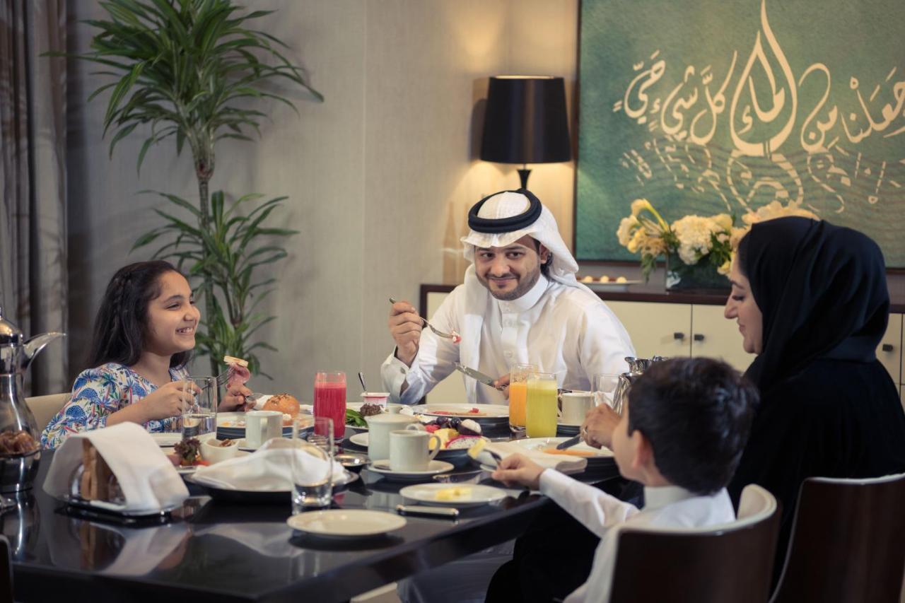 Hotel Jabal Omar Hyatt Regency Makkah Mekka Zewnętrze zdjęcie The photo depicts a cheerful family gathered around a dining table for a meal. They appear to be enjoying breakfast or a brunch. The table is set with various dishes and drinks, including juices and plates of food. 

A man wearing traditional attire 