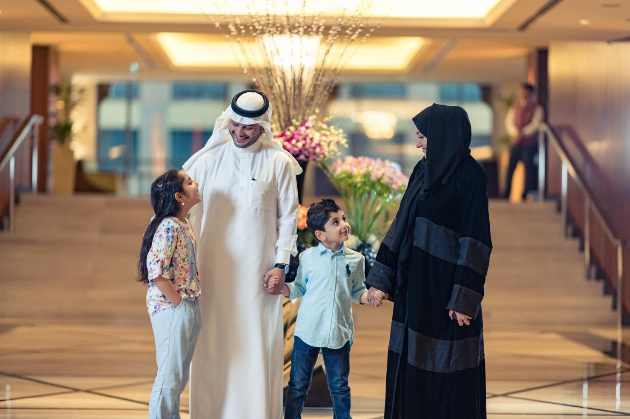 Hotel Jabal Omar Hyatt Regency Makkah Mekka Zewnętrze zdjęcie The photo shows a family in a hotel lobby. There are two children, a boy and a girl, standing between their parents. The girl is smiling and looking up at her father, who is wearing traditional white attire and a headscarf. The boy is also smiling an