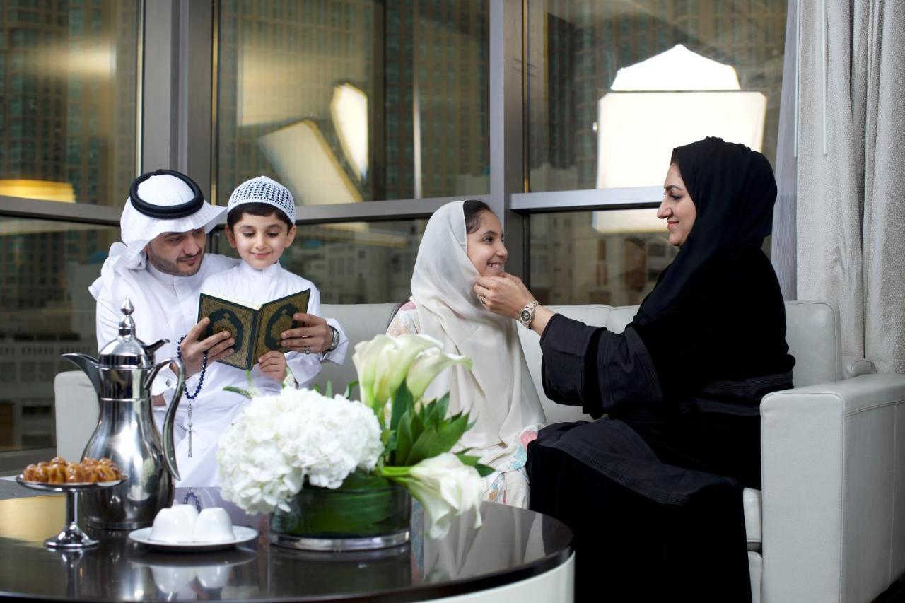 Hotel Jabal Omar Hyatt Regency Makkah Mekka Zewnętrze zdjęcie The photo depicts a family gathering in a modern, well-furnished setting. A man and a boy, both dressed in traditional attire, are engaged in reading from a book, likely the Quran. A woman, wearing a hijab and a black abaya, is sitting next to them, 