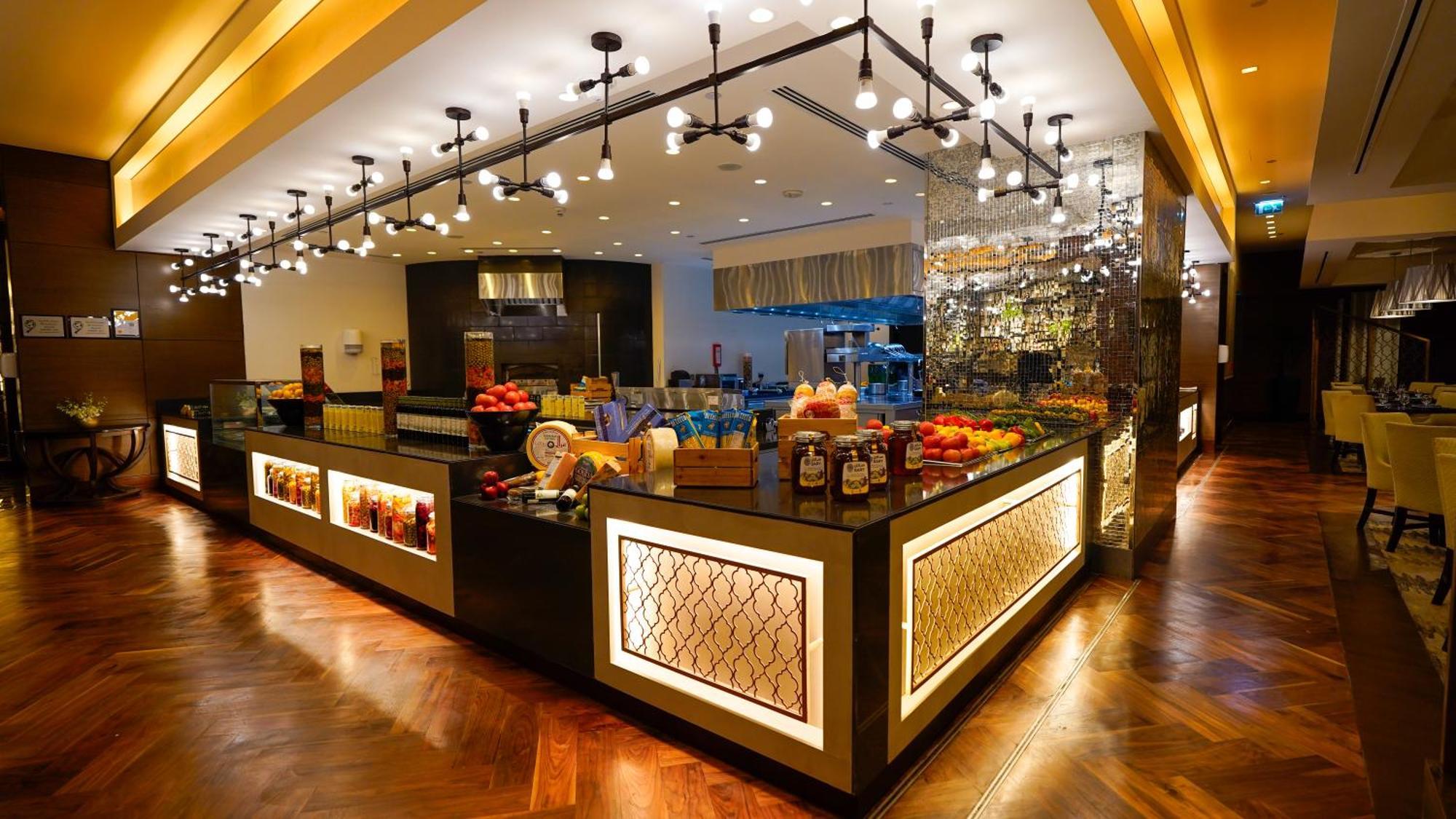 Hotel Jabal Omar Hyatt Regency Makkah Mekka Zewnętrze zdjęcie The photo shows a stylish and modern buffet area in a restaurant or hotel. The design features a sleek counter with various food items displayed, including fresh fruits. The space is well-lit with pendant lights hanging from the ceiling, creating a w