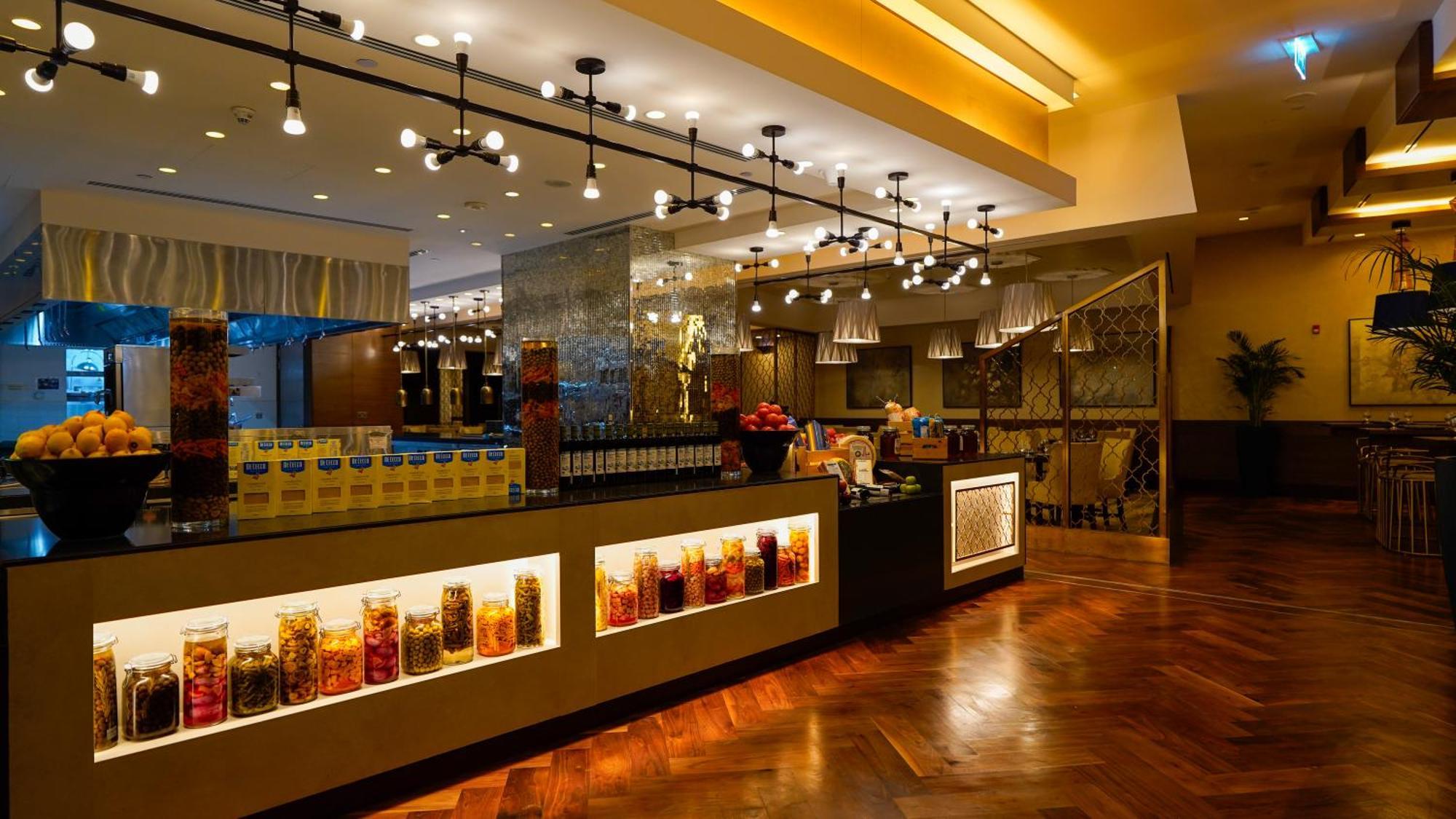 Hotel Jabal Omar Hyatt Regency Makkah Mekka Zewnętrze zdjęcie The photo shows a stylish interior of a restaurant or café. It features a well-lit space with modern lighting fixtures hanging from the ceiling. The focal point is a counter area with jars filled with colorful ingredients or snacks, illuminated by li