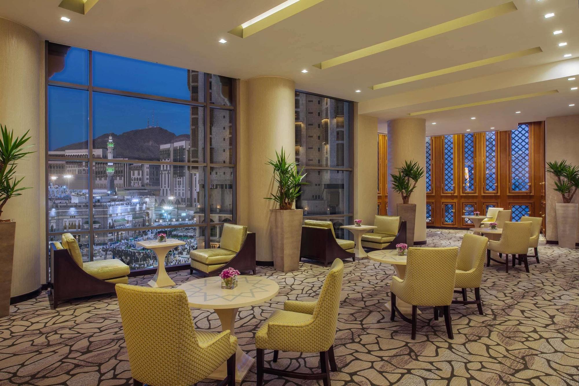 Hotel Jabal Omar Hyatt Regency Makkah Mekka Zewnętrze zdjęcie The photo shows a stylish lounge area, likely located in a hotel or café. It features several comfortable seating arrangements with light-colored chairs and small tables. The space is well-lit with modern lighting and has large windows that offer a v