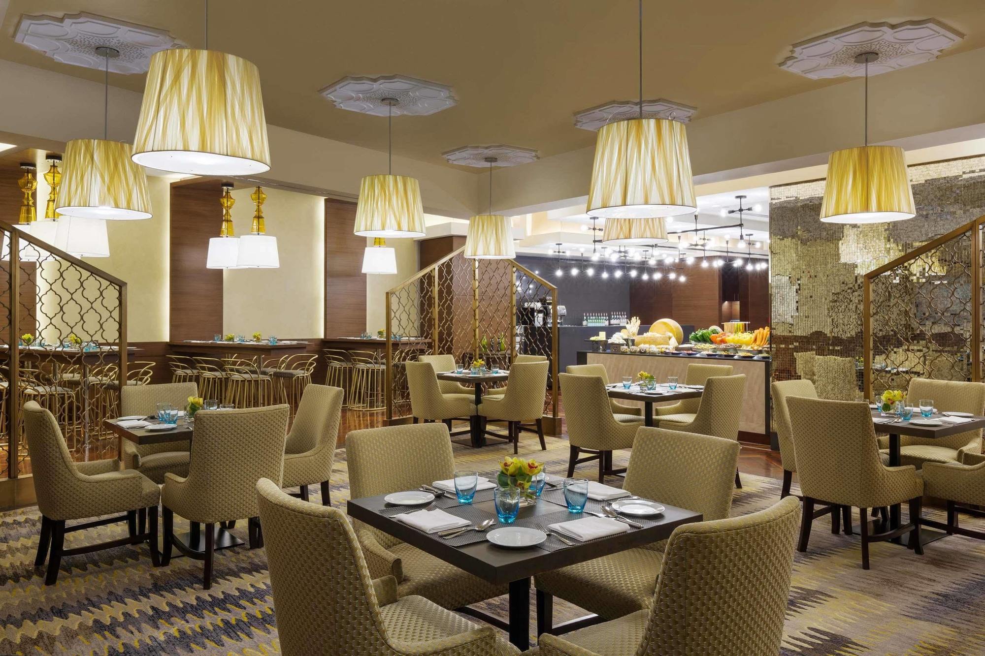 Hotel Jabal Omar Hyatt Regency Makkah Mekka Zewnętrze zdjęcie The photo displays a modern restaurant interior. It features a series of round tables with beige upholstered chairs arranged neatly throughout the space. Each table is set with plates and blue-tinted glasses. The lighting is provided by stylish penda