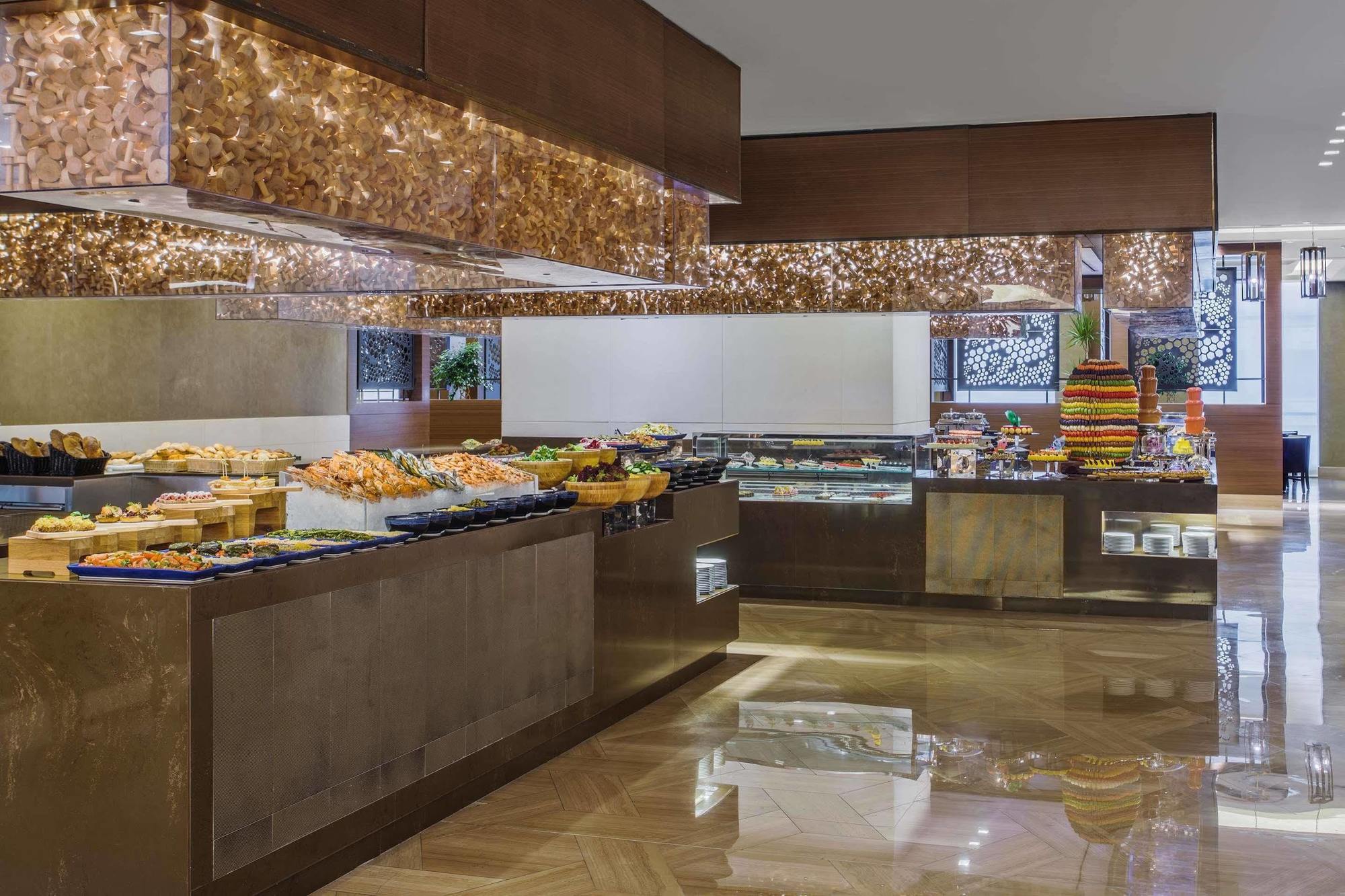 Hotel Jabal Omar Hyatt Regency Makkah Mekka Zewnętrze zdjęcie The photo shows an elegant buffet setup in a spacious dining area. There are various food displays arranged on sleek surfaces, including an assortment of items such as pastries, fruits, and possibly other dishes. The decor features warm lighting with
