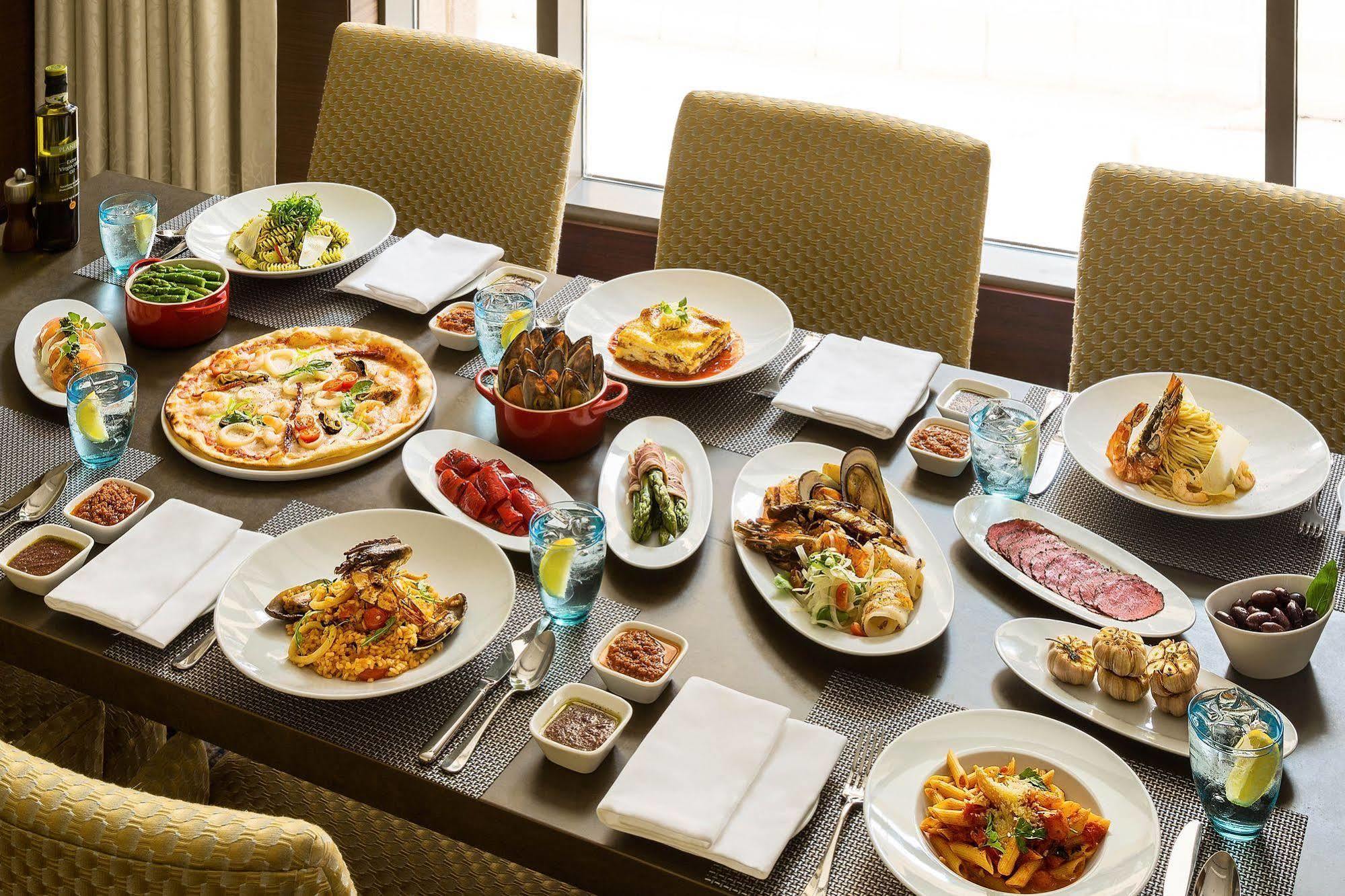 Hotel Jabal Omar Hyatt Regency Makkah Mekka Zewnętrze zdjęcie The photo shows a large dining table set with various dishes, suggesting a festive or communal meal. There are several plates of food including:

- A pizza topped with vegetables and possibly meats.
- A serving of lasagna.
- A variety of pasta dishes