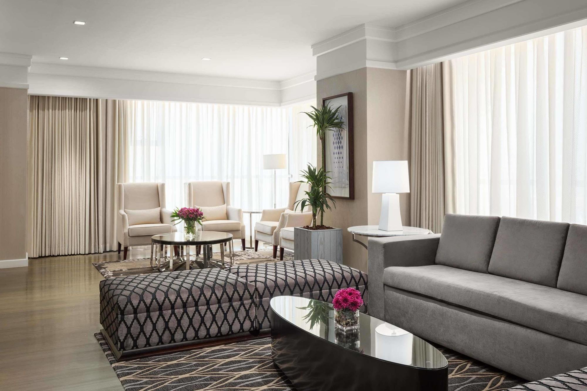 Hotel Jabal Omar Hyatt Regency Makkah Mekka Zewnętrze zdjęcie The photo depicts a modern living room with a stylish and inviting design. There are large windows covered with light-colored curtains that allow natural light to fill the space. The furniture includes a gray sofa, a patterned ottoman with a geometri