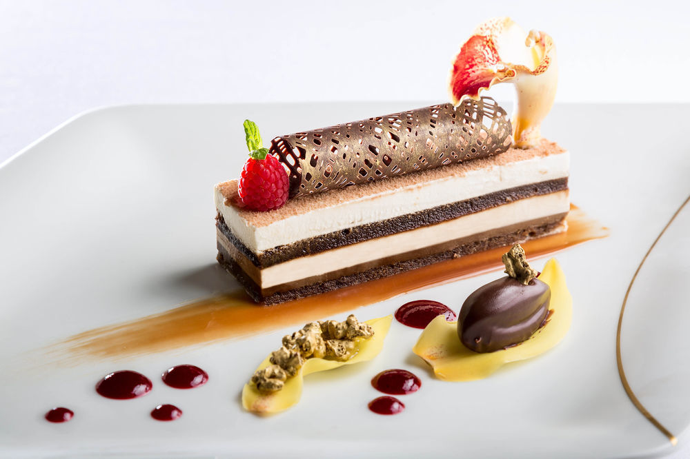 Hotel Jabal Omar Hyatt Regency Makkah Mekka Zewnętrze zdjęcie The photo showcases an elegantly plated dessert. It features a layered cake with different textures and flavors, including chocolate and cream layers. The dessert is topped with a decorative chocolate tube and garnished with fresh raspberries and a s
