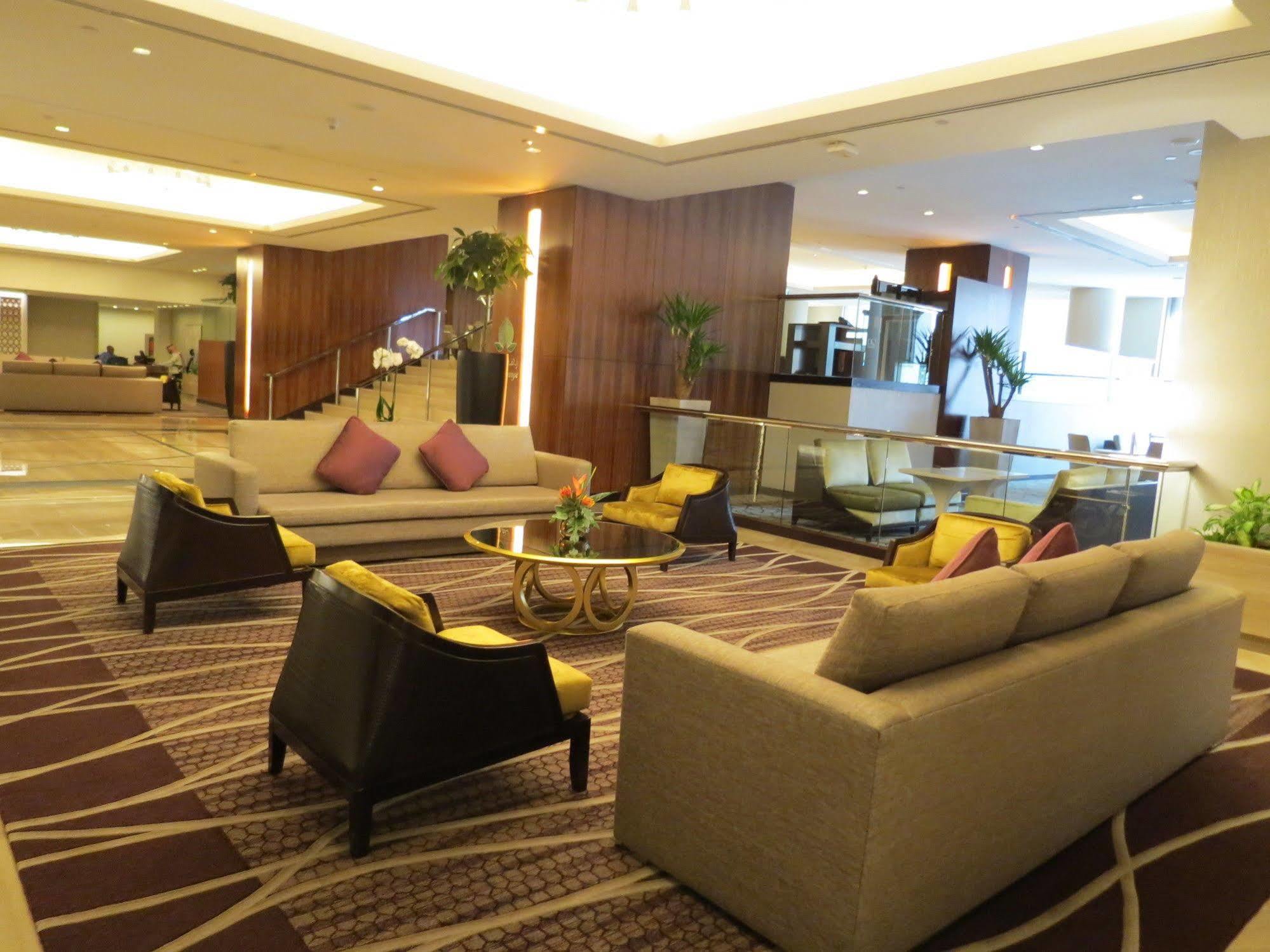 Hotel Jabal Omar Hyatt Regency Makkah Mekka Zewnętrze zdjęcie The photo shows a modern and stylish lobby or lounge area. It features two large sofas with a light color and several cushions in shades of purple. There are also two armchairs with a darker finish and yellow cushions. In the center, there is a round