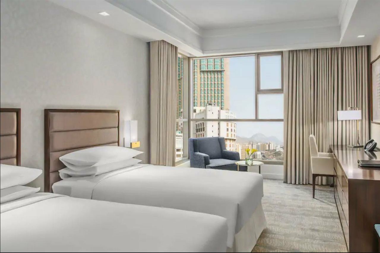 Hotel Jabal Omar Hyatt Regency Makkah Mekka Zewnętrze zdjęcie The photo shows a modern hotel room featuring two beds with white linens. The room has a bright and airy feel, thanks to large windows that allow natural light to flood in. There are floor-to-ceiling curtains, and a small seating area with a chair an