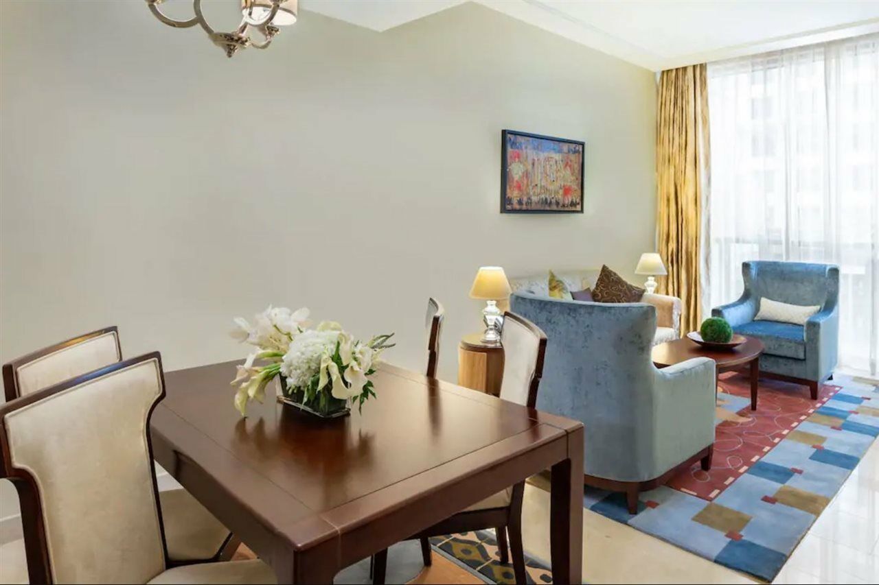 Hotel Jabal Omar Hyatt Regency Makkah Mekka Zewnętrze zdjęcie The photo shows an elegantly furnished living space. On the left, there's a wooden dining table with four chairs, decorated with a vase of white flowers. To the right, there are two comfortable blue armchairs and a small side table, each adorned with